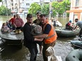 Volunteers help to unload a disabled local resident from a boat during an evacuation from a flooded area in Kherson on June 8, 2023, following the blowing of the dam at Ukraine's Kakhovka hydroelectric power plant dam.